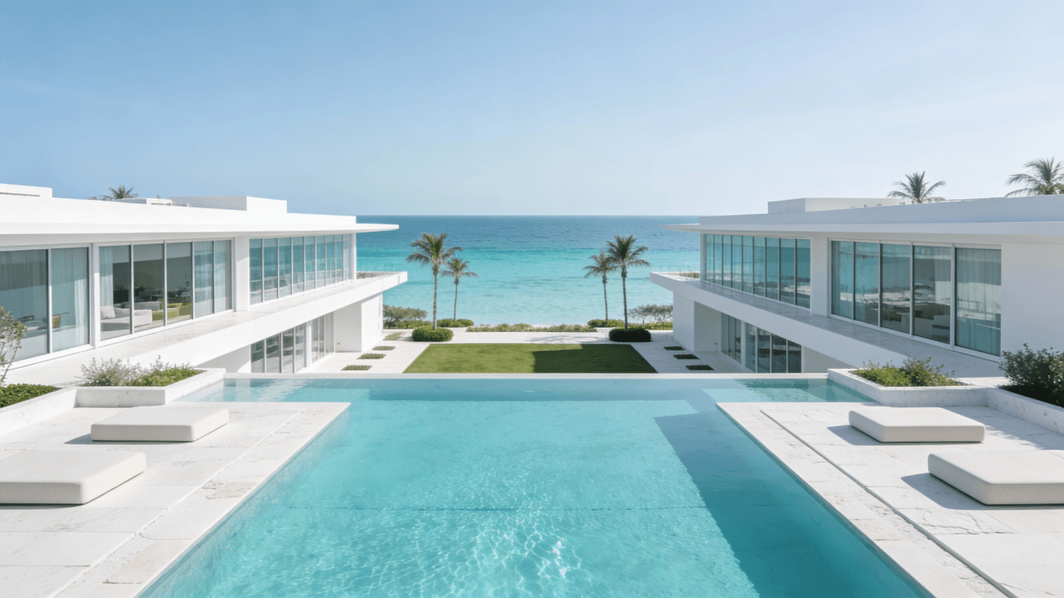 White villa architecture framing a long turquoise pool that leads towards palm trees and the open sea
