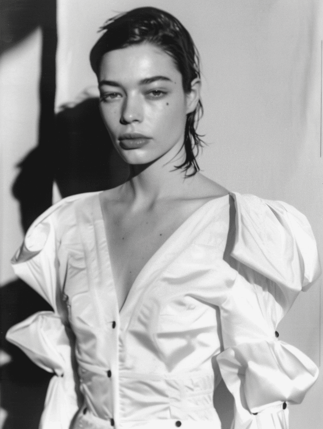 Black and white editorial portrait of a woman in a sculptural white blouse with a strong shadow behind her
